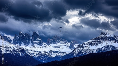 A paraglider soars over a snow-capped mountain range.