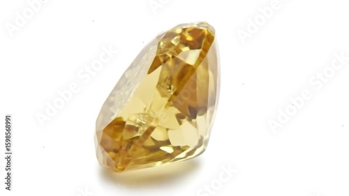 A single, cut yellow diamond rests on a white surface, showcasing its facets and internal reflections.