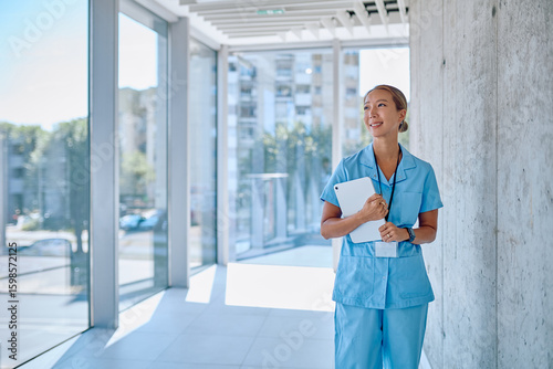 Bild auf Leinwand Portrait of a smiling asian female doctor in blue scrubs holding a tablet while