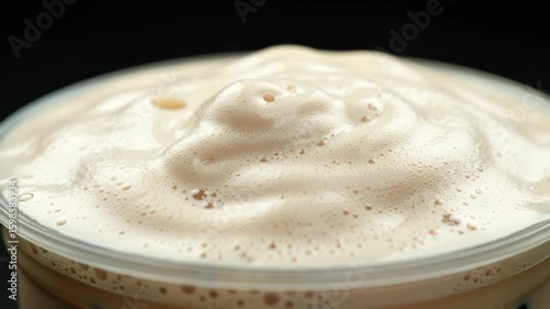 Pouring iced coffee drink with frothy foam in plastic cup close up.
