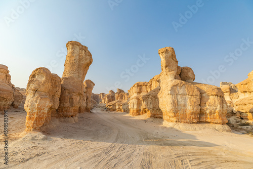 Wind-sculpted sandstone formations rise from the desert floor in Jabal Al Qarah, Al Ahsa, Saudi Arabia, creating a mesmerizing landscape under the clear blue sky