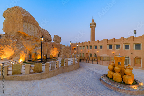 Illuminated rock caves and mosque of Jabal Al Qarah mountain with fountain at dusk in Al Ahsa oasis, Saudi Arabia, showing local culture and heritage