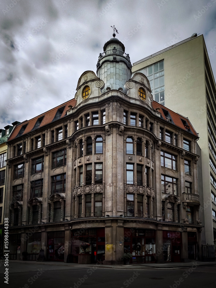 Fototapeta premium A historic corner building with dome and ornate facade rises under a cloudy sky in the city center.