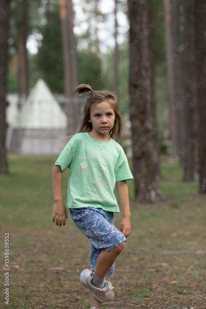 Fototapeta premium a girl child walking in a pine forest, one leg bent, looking into the distance