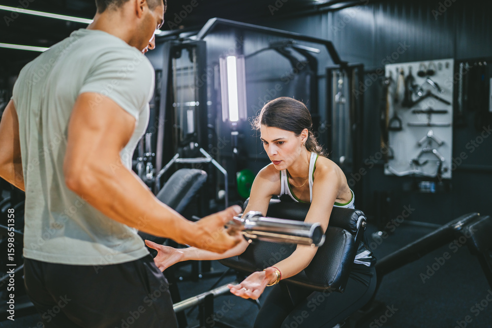 Obraz premium woman do biceps curls exercising while personal trainer spotting her