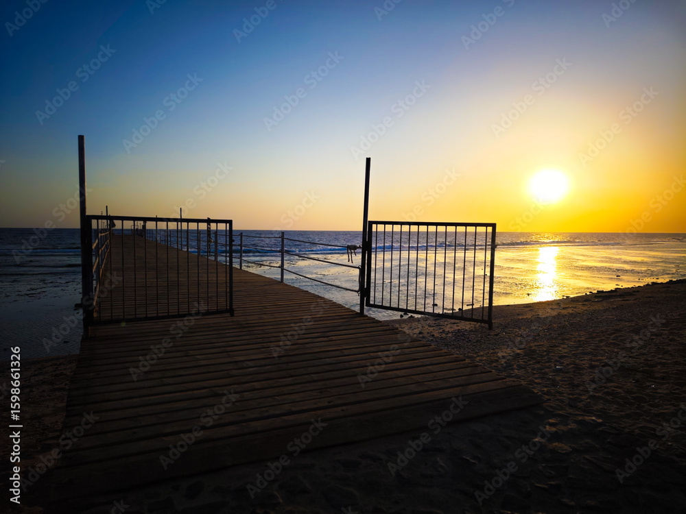 Fototapeta premium An open gate leads to the sea in the setting sun – a symbol of freedom and openness.
