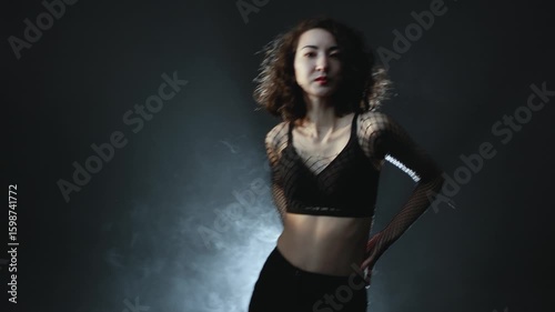 Modern dance, a young woman dancing on a dark background, atmospheric lighting in smoke. A girl in black pants and a mesh blouse performs modern movements in heels