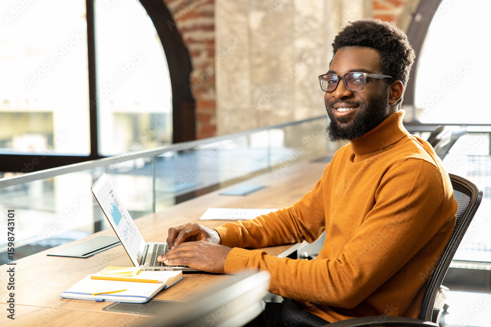 Obraz premium African american young man with laptop working in the office
