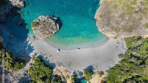 Aerial view of a secluded pebble beach surrounded by rocky cliffs and lush greenery, with crystal clear turquoise waters. Ideal summer travel destination. Foneas beach - Messiniaki Mani