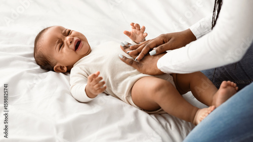 Obraz na płótnie Displeased black baby crying and whining, feeling colic or abdomen ache, lying on back in bed
