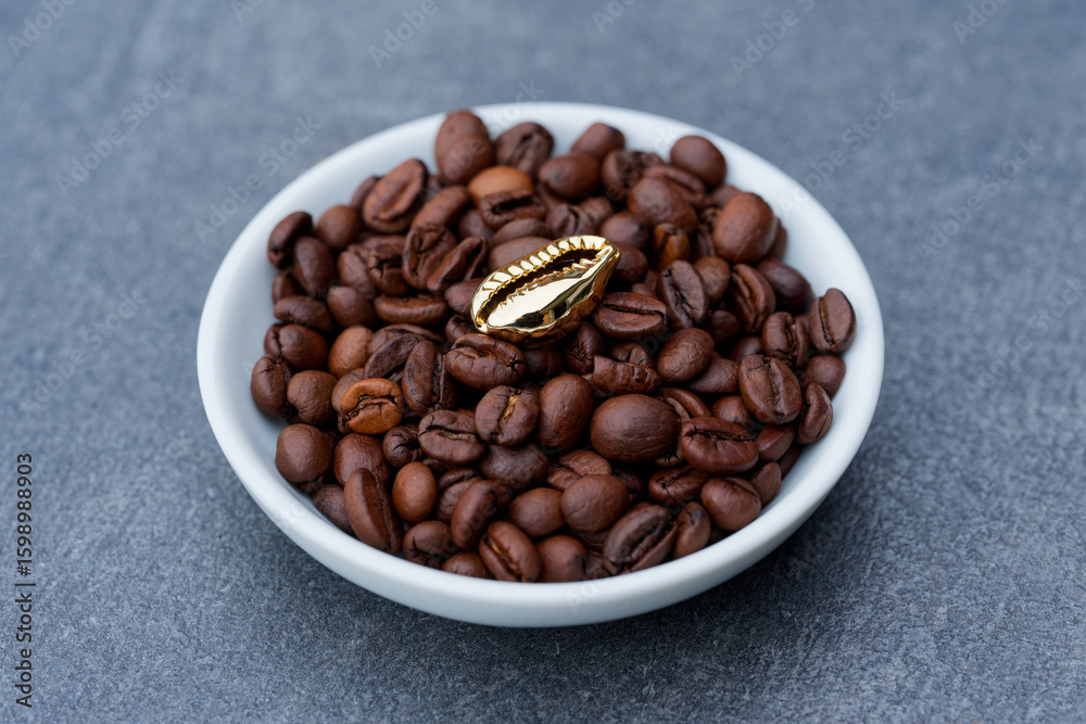 Fototapeta premium Coffee beans in a bowl with a golden bean on top with a gray background