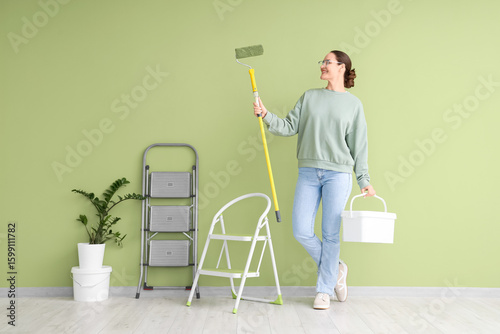 Young woman with paint roller and stepladder near green wall