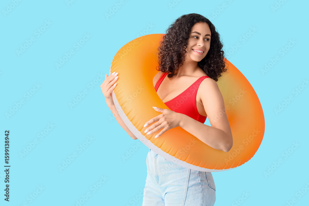 © Pixel-Shot - Young African-American woman with orange inflatable ring on blue background © Pixel-Shot - Young African-American woman with orange inflatable ring on blue background