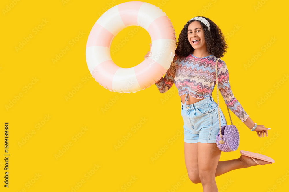 Young African-American woman with inflatable ring on yellow background Young African-American woman with inflatable ring on yellow background