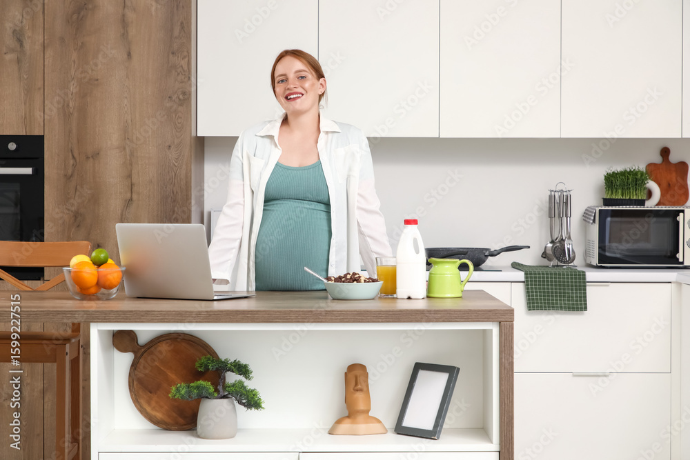 Young pregnant woman with laptop and breakfast in kitchen Young pregnant woman with laptop and breakfast in kitchen