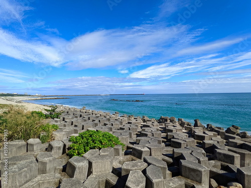 A beach half-filled with tetrapod and sandy at the other side facing the Pacific Ocean with a lighthouse in sight under a sunny blue sky during the pandemic