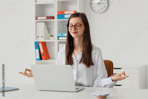 Young businesswoman meditating at table in office