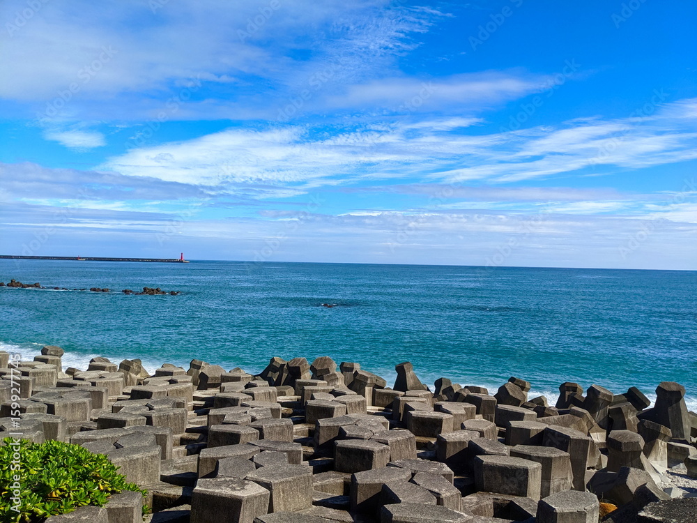 Fototapeta premium A beach filled with tetrapod facing the Pacific Ocean with a lighthouse in sight under a sunny blue sky during the pandemic