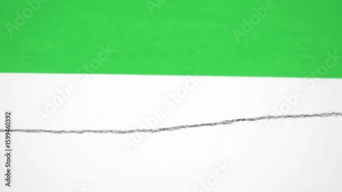 A pencil drawing a gray line on a white surface with a blurred green background