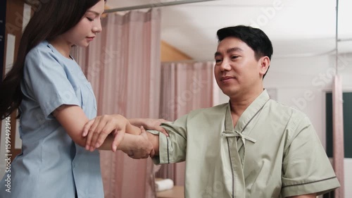 Male Asian patient is hand stretching, treated for health recovery for muscle pain relief by female physical therapist doctor, passive medical therapy at spa clinic, and wellness massaging healthcare.