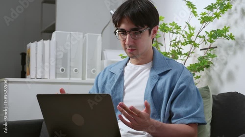 Young caucasian man working remote in home office, using laptop computer during video call meeting, digital nomad, male video call for small business planning in living room, online collaboration.