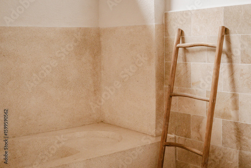 Empty bathroom interior with a bathtub and bamboo towel rack made of natural materials and light colours like beige and sand colour inside a hotel room at daytime during summer holiday in Bali.