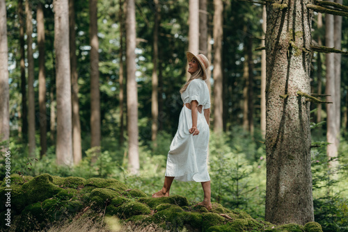 Quadro em tela Woman in straw hat and white dress leaps playfully in forest, escaping daily str