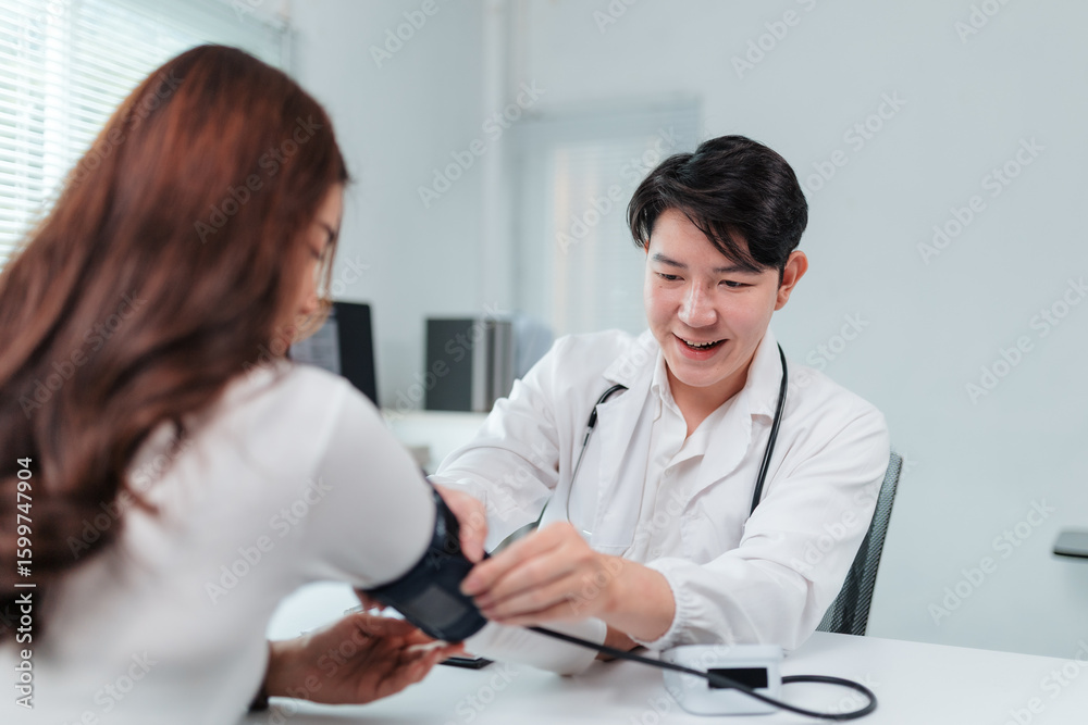 Obraz premium Smiling doctor using sphygmomanometer checking blood pressure of patient during medical exam in hospital office, healthcare and medical concept