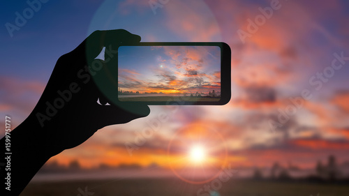 Silhouette hand holding smartphone photograph sunset