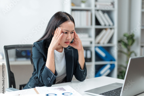 Obraz na plátně Young Asian manager touching her temples while working on a laptop in a modern o