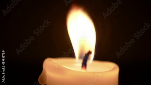 A single, lit candle glowing with a warm, bright flame against a completely dark background. A symbol of hope, peace, and remembrance.
