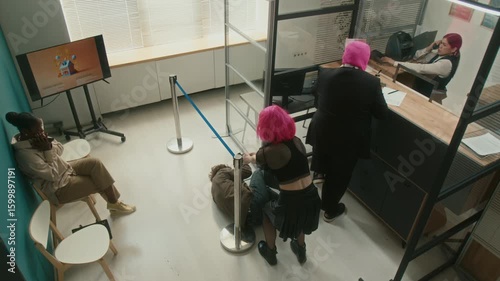 High angle shot of female and male robbers disguised by pink wig and balaclava breaking into bank threatening scared customers and teller with guns demanding money