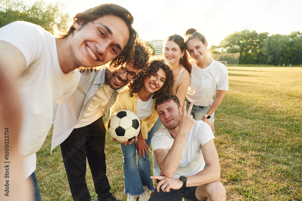Obraz premium Handsome man is doing a selfie. Young friends are having fun on the field with soccer ball