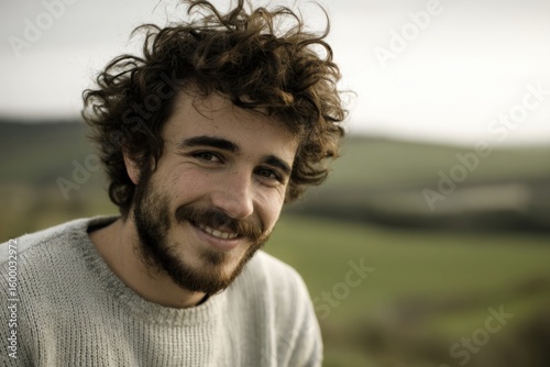 Young man smiling outdoors in a natural green field landscape during daytime.