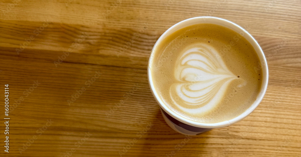 Obraz premium A beautifully crafted cappuccino sits on a wooden table, showcasing intricate latte art with heart shapes atop creamy foam.