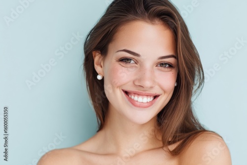 Close-up portrait of a cheerful young woman with brown hair smiling against pastel background.