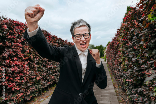 Businesswoman in suit celebrating outdoors beside green wall