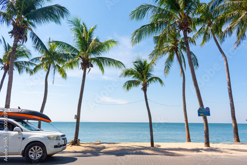 Fototapeta Naklejka Na Ścianę i Meble -  Bang-Saen Beach has palm trees sway gently against a backdrop of blue sky and sea, with a car parked under palm trees with a boat on top. Chon Buri, Thailand