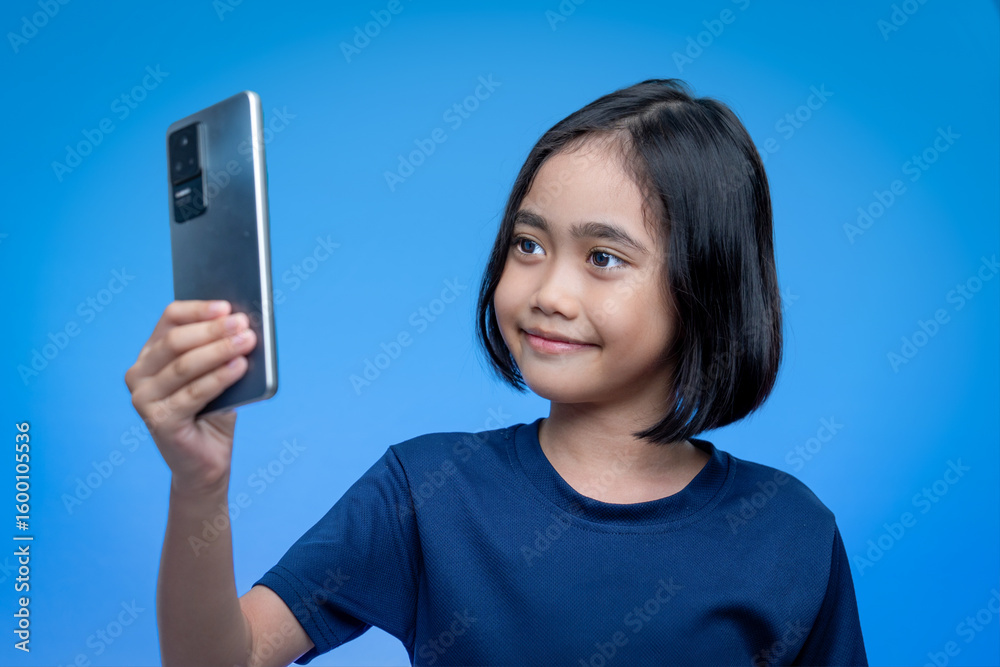 A young Asian girl holding a smartphone up to take a selfie or record a video. Modern childhood and digital interaction concept. A young Asian girl holding a smartphone up to take a selfie or record a video. Modern childhood and digital interaction concept.