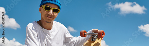 Fotografie Smiling young man with skateboard enjoys a sunny day at the park under blue skie