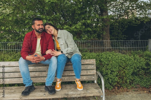 Happy couple sits on a bench outdoors, smiling and hugging each other. A joyful, affectionate moment capturing love, connection, and carefree togetherness in a relaxed, natural setting