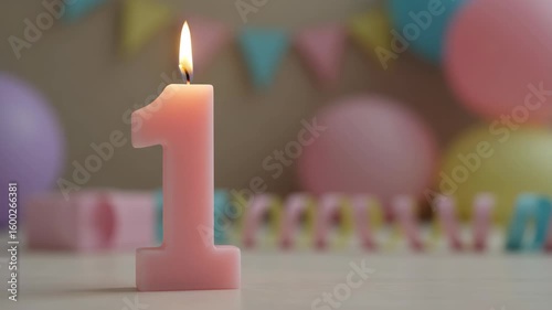 Pink number one candle burning on table with party decorations  