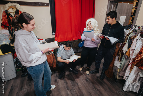 Fotografija Actors actively engaging in a rehearsal scene, studying scripts, and discussing performance details, surrounded by theater costumes