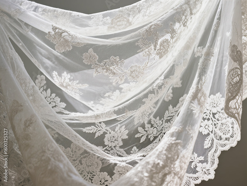 Delicate white lace fabric with a close-up floral pattern. The folds in the lace fabric create elegant texture and depth for wedding and fashion designs.