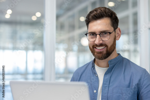 A smiling, bearded man with glasses looks directly at the camera. He wears a blue shirt and is in an office setting. Free Download A smiling, bearded man with glasses looks directly at the camera. He wears a blue shirt and is in an office setting. - GFXLoad