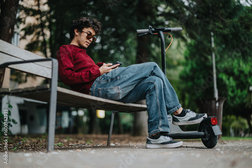 Photos A young man wearing sunglasses is sitting and relaxing on a park bench, using his phone