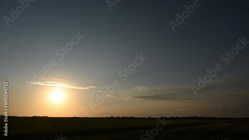 Timelapse looking towards the sun at sunrise with scattered colorful clouds moving above a flat prairie landscape
