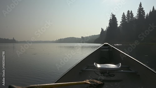 View from a canoe drifting on a calm lake covered in wildfire smoke with evergreen trees along the shore
