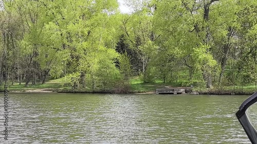 A serene escape unfolds with lush green trees lining the peaceful lakeside. The calm water reflects the vibrant foliage, offering a perfect sanctuary for nature lovers and adventurers alike.