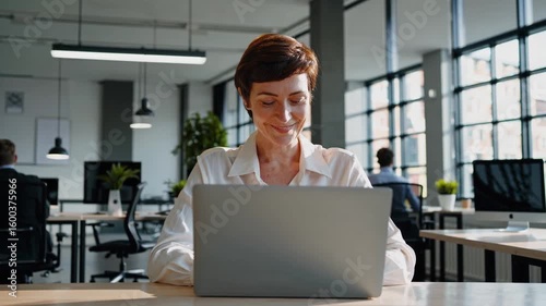 Smiling woman working at a laptop in a modern office setting during the day